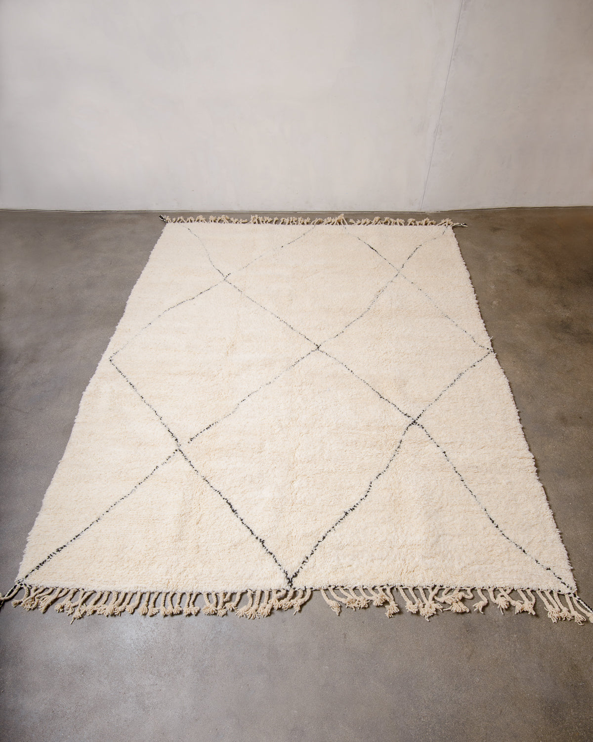 Cream Beniourain rug laid flat on concrete floor in front of a white wall.